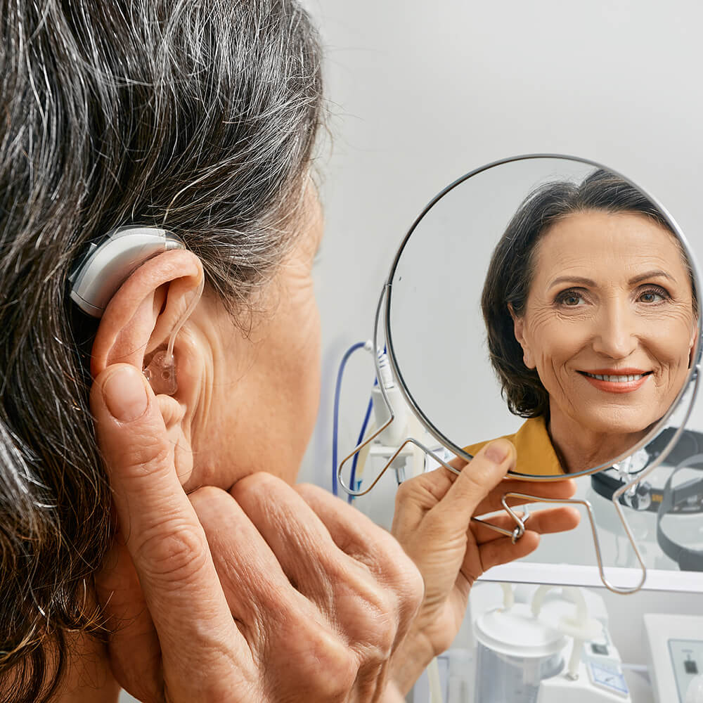 woman looks in mirror while wearing hearing aid